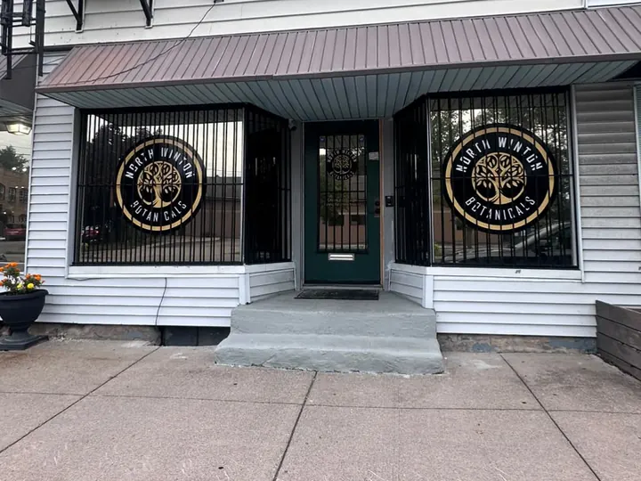 North Winton Botanicals storefront on East Main Street in Rochester, NY, with the gold badge in both windows and a green front door